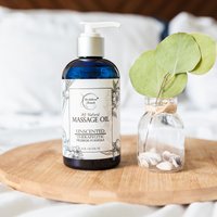 Image of Unscented Almond Massage Oil on a wooden board with decorations next to it.