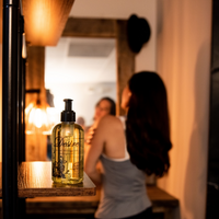 Desire Sensual Massage Oil showcased on a wooded shelf, with a woman in the background.