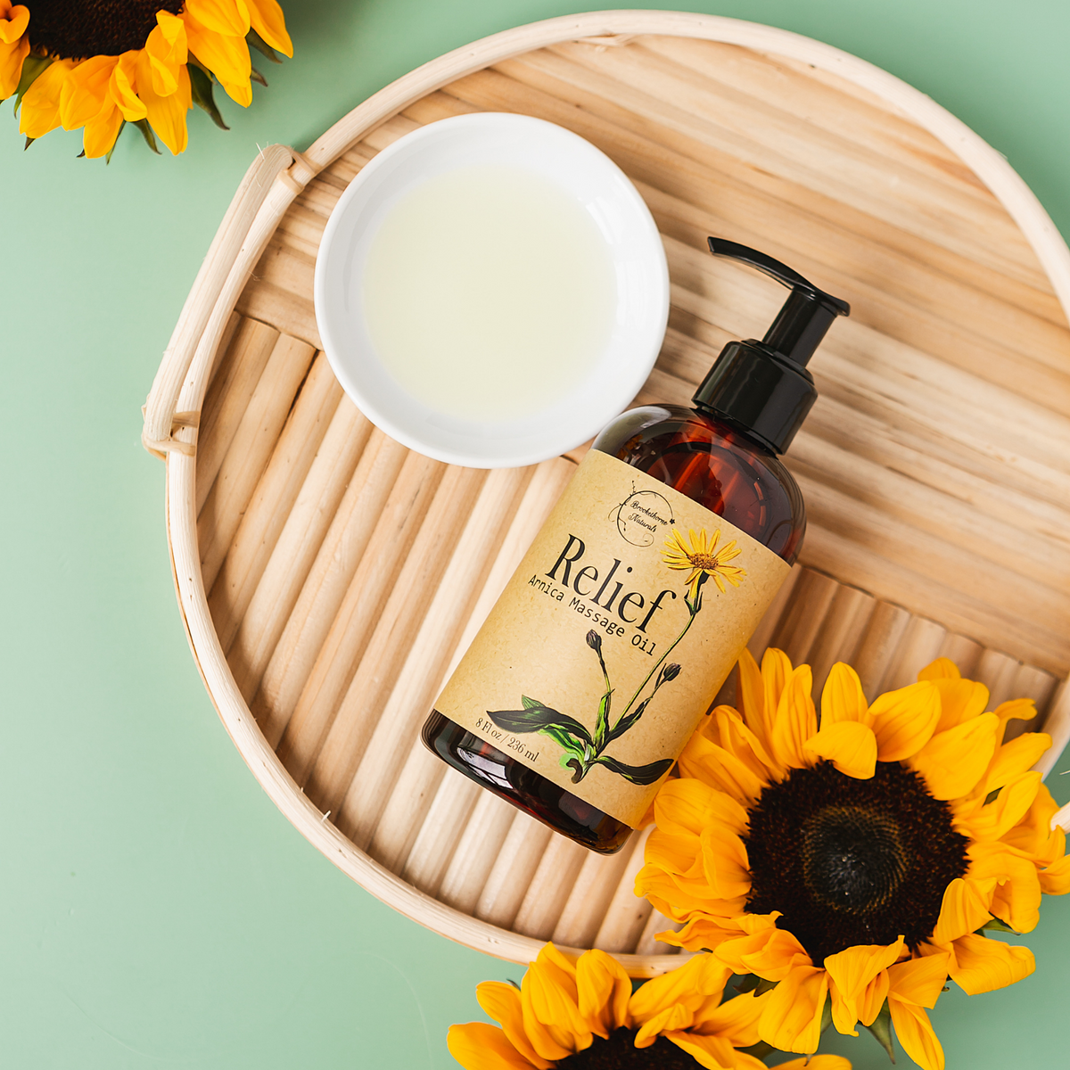 Relief Arnica Massage Oil on a wicker board with a bowl of oil and sunflowers