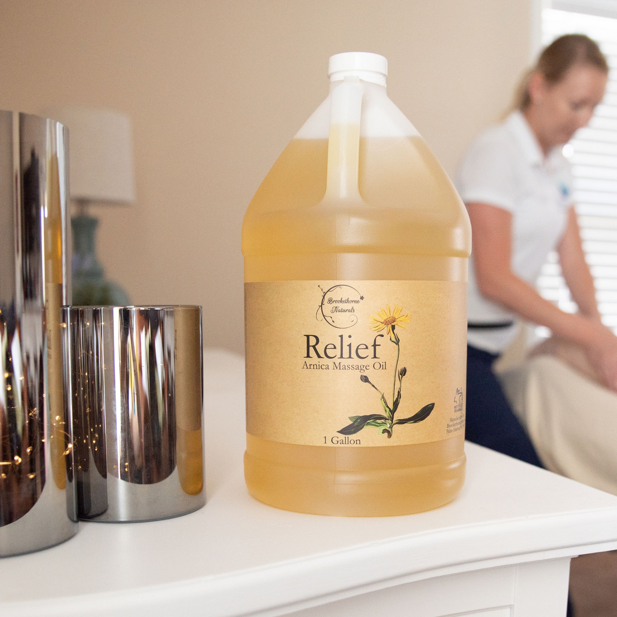 Relief Arnica Massage Oil 1 Gallon Jug, with a massage therapist in the background