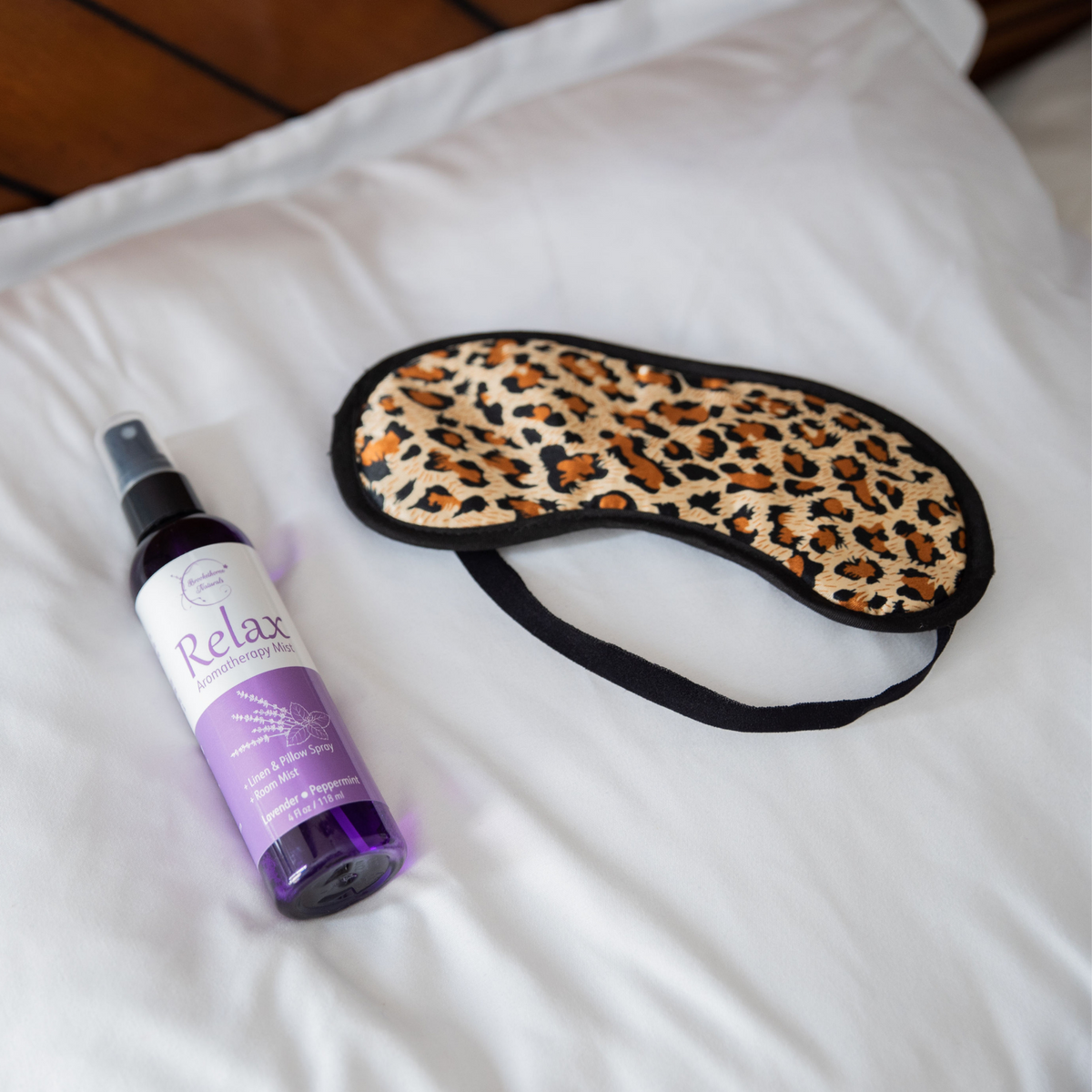 Relax Aromatherapy Mist laying on a pillow next to a cheetah printed sleep mask