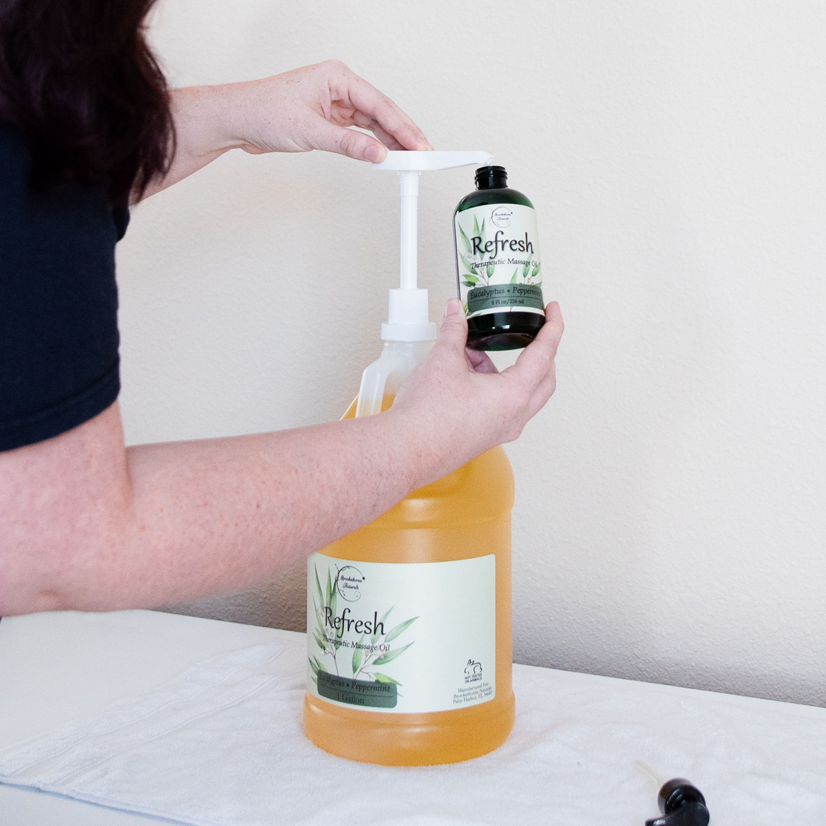 Refresh Massage Oil being pumped from a gallon jug into an 8oz bottle