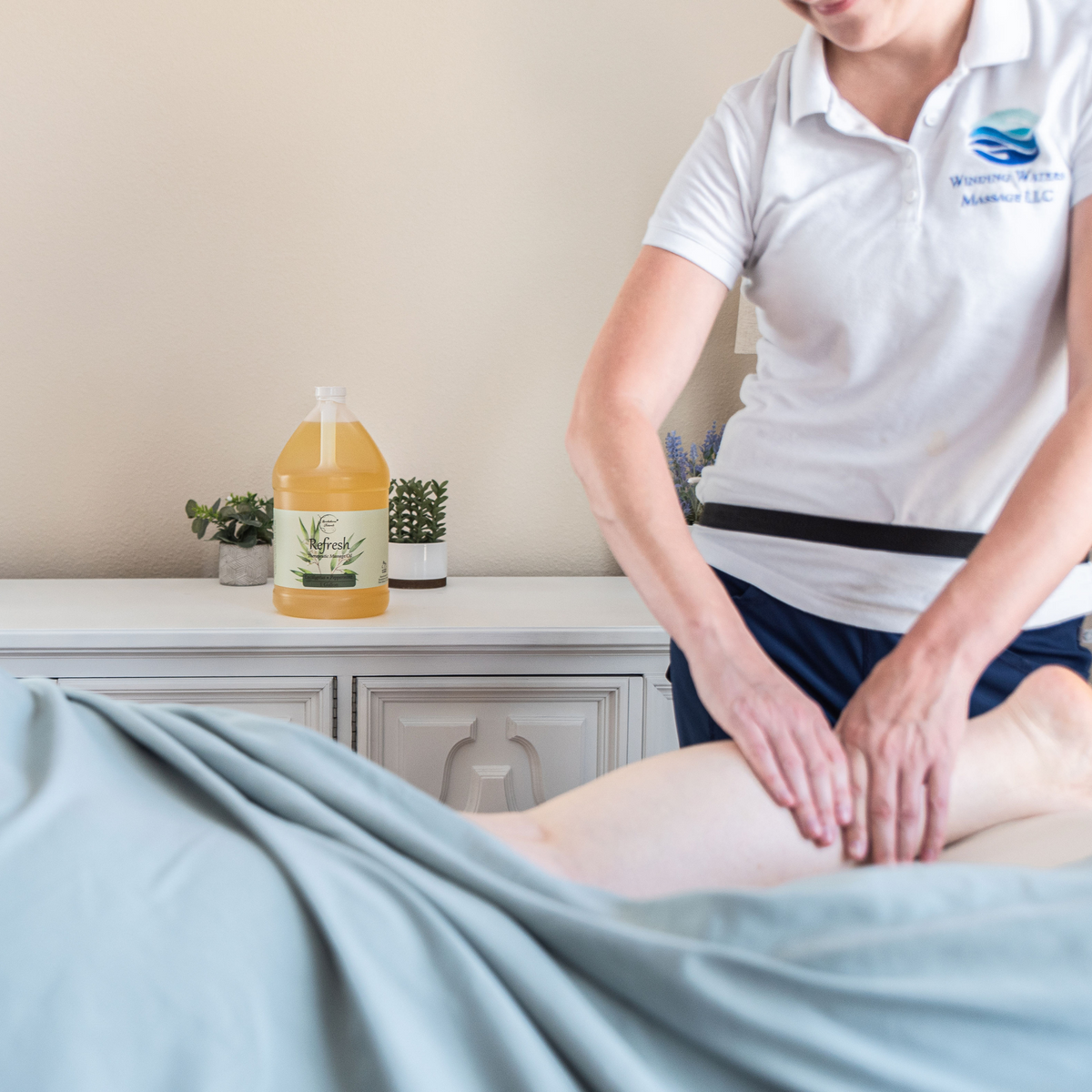 Person receiving a professional massage with Refresh Massage Oil, gallon jug is showcased in the background